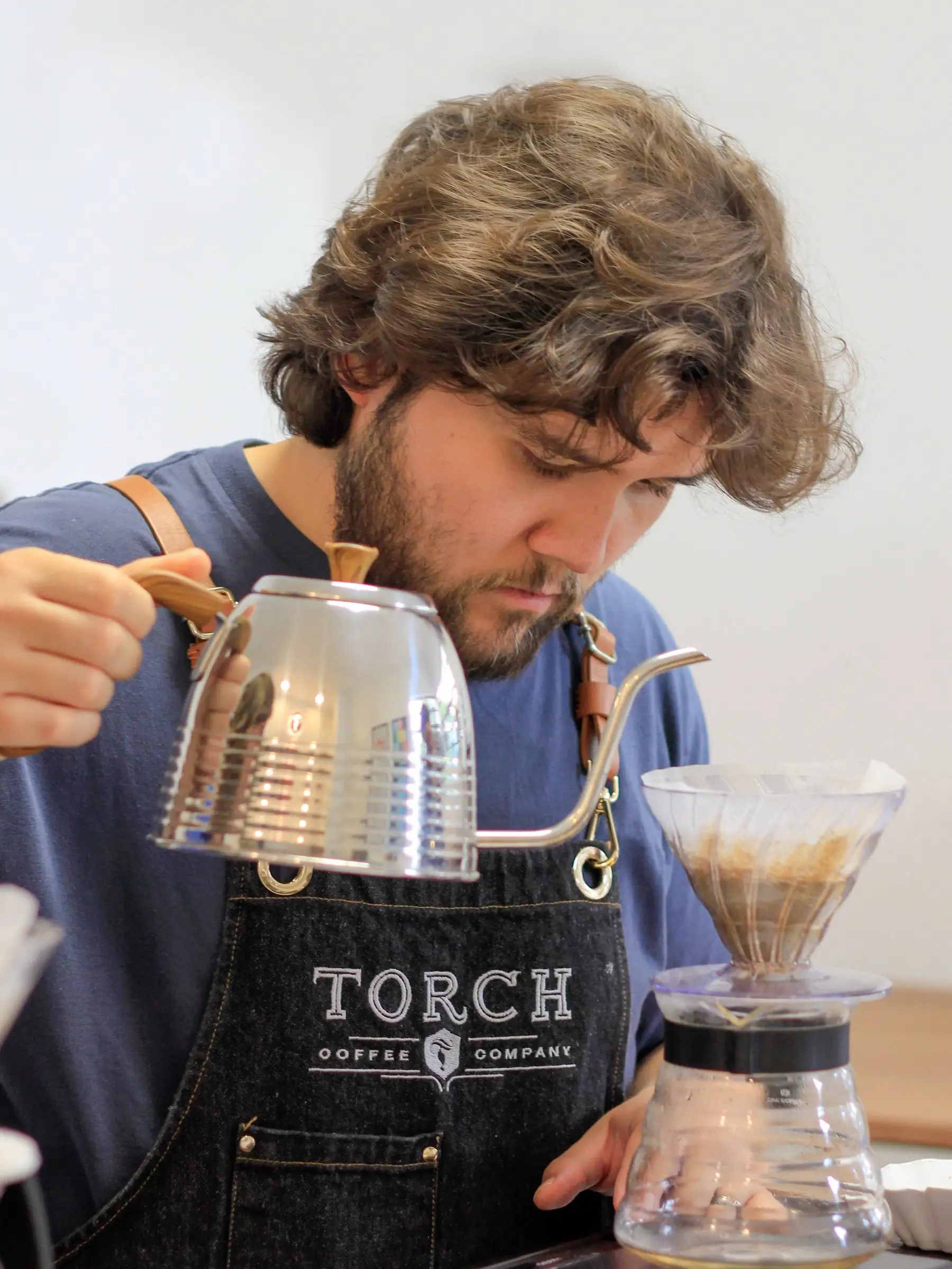 Barista con delantal de Torch preparando un filtrado con tetera de cuello de cisne