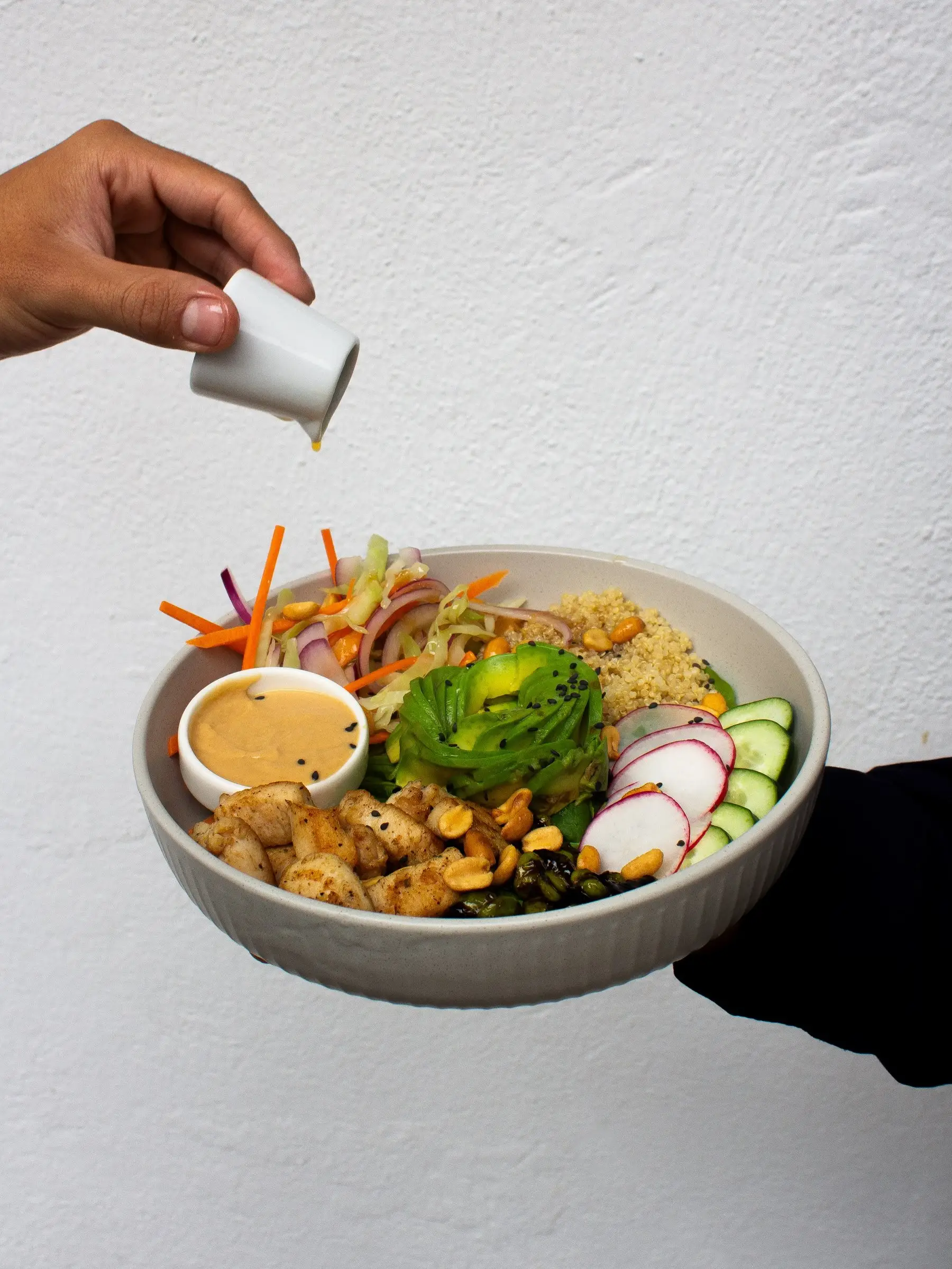 Bowl Umami con pollo satay, quinoa, aguacate, rábano y aderezo de maní servido en la mano