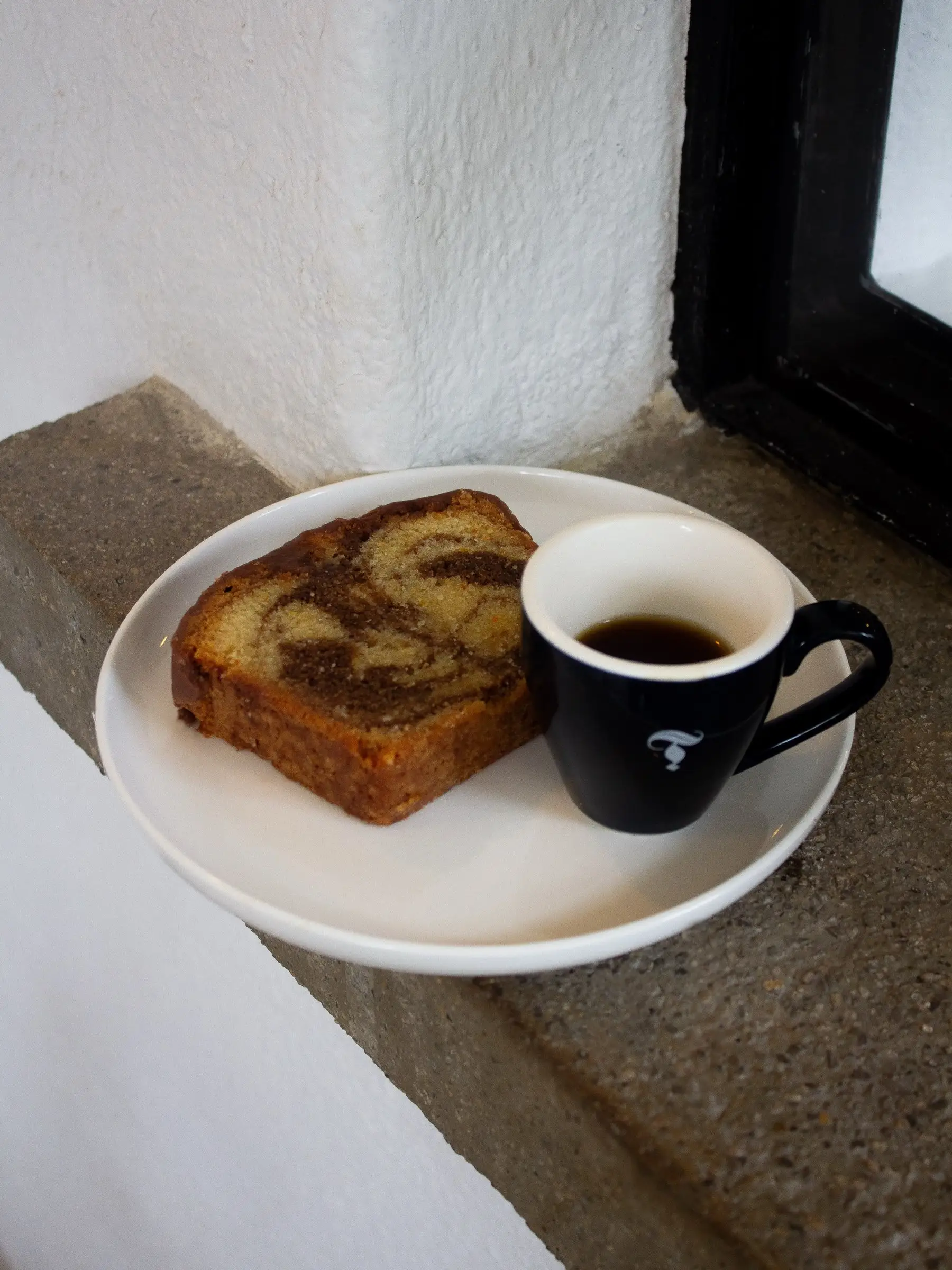 Espresso en taza negra de Torch junto a una rebanada de pan marmoleado