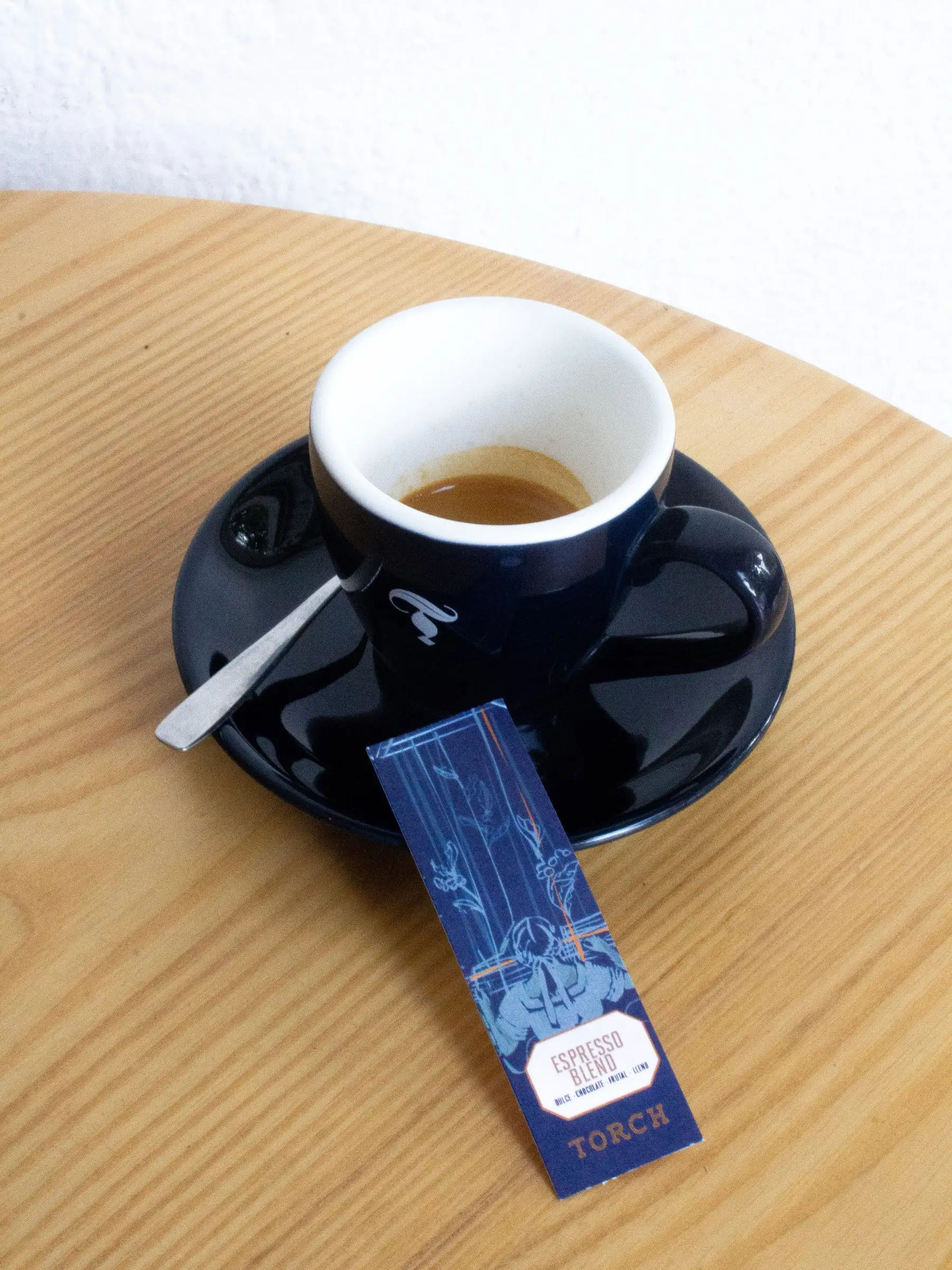 Espresso en taza azul de Torch sobre su plato, con la tarjeta del Espresso Blend apoyada al lado, en una mesa de madera